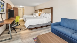 Habitación de hotel con dos camas, un escritorio con computadora, un sofá azul y una alfombra pequeña.