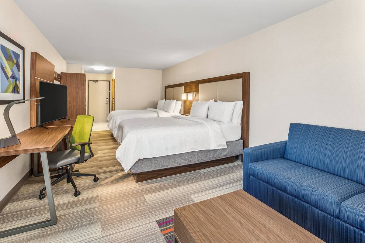A hotel room with two beds, a desk with a computer, a blue sofa, and a small rug.