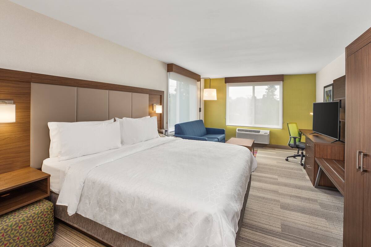 A hotel room with a large bed, a desk, a chair, and a television.