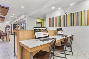 A modern reception desk with two computer monitors, a coffee station, and a colorful striped wall. - Holiday Inn Express & Suites Tacoma by IHG (Tacoma)
