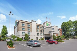 A multi-story hotel with a prominent Holiday Inn Express sign, a parking lot with several cars, and a clear blue sky.