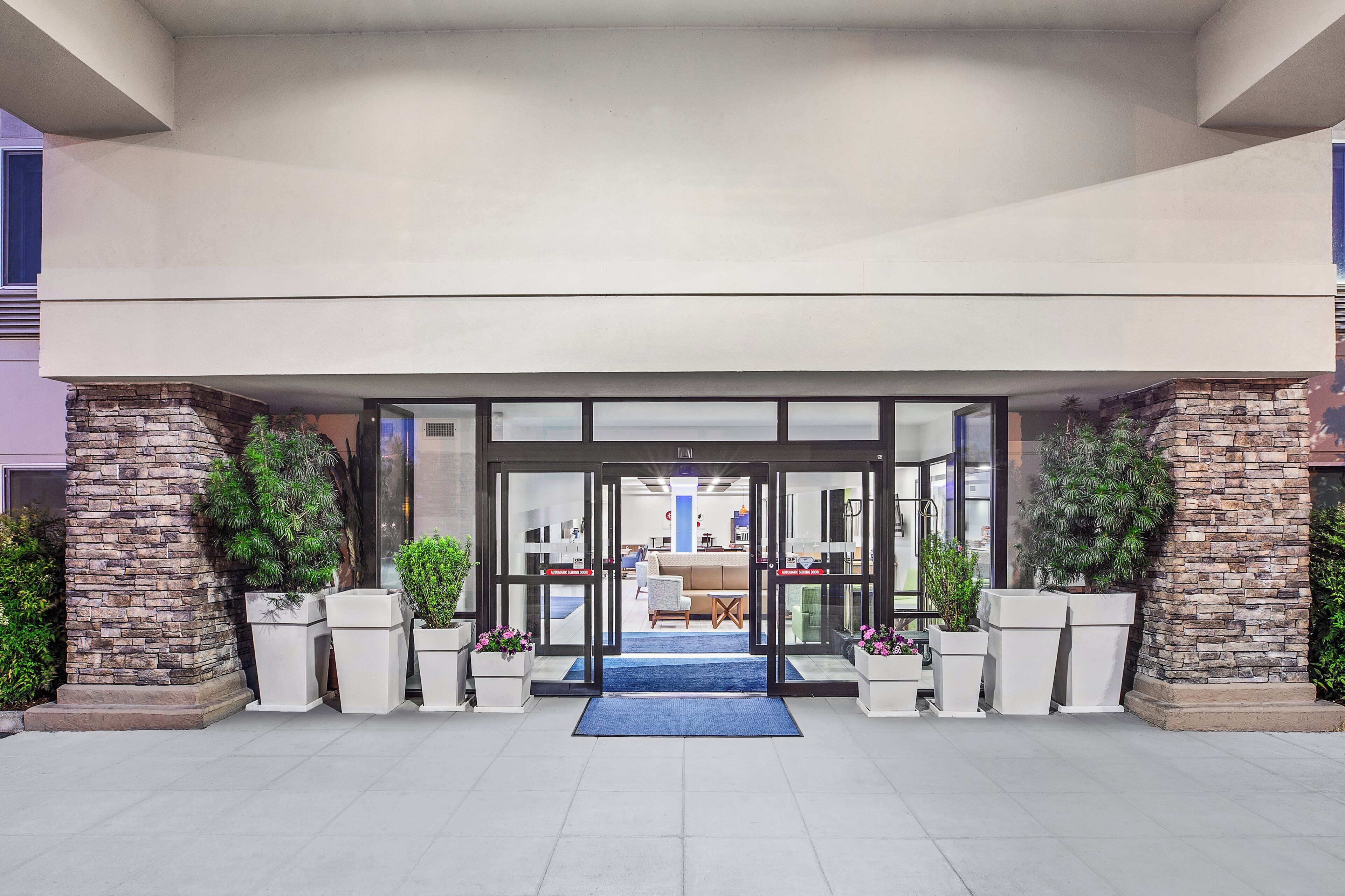 L’entrée d’un hôtel, avec une porte en verre, des piliers en pierre et des plantes en pot.