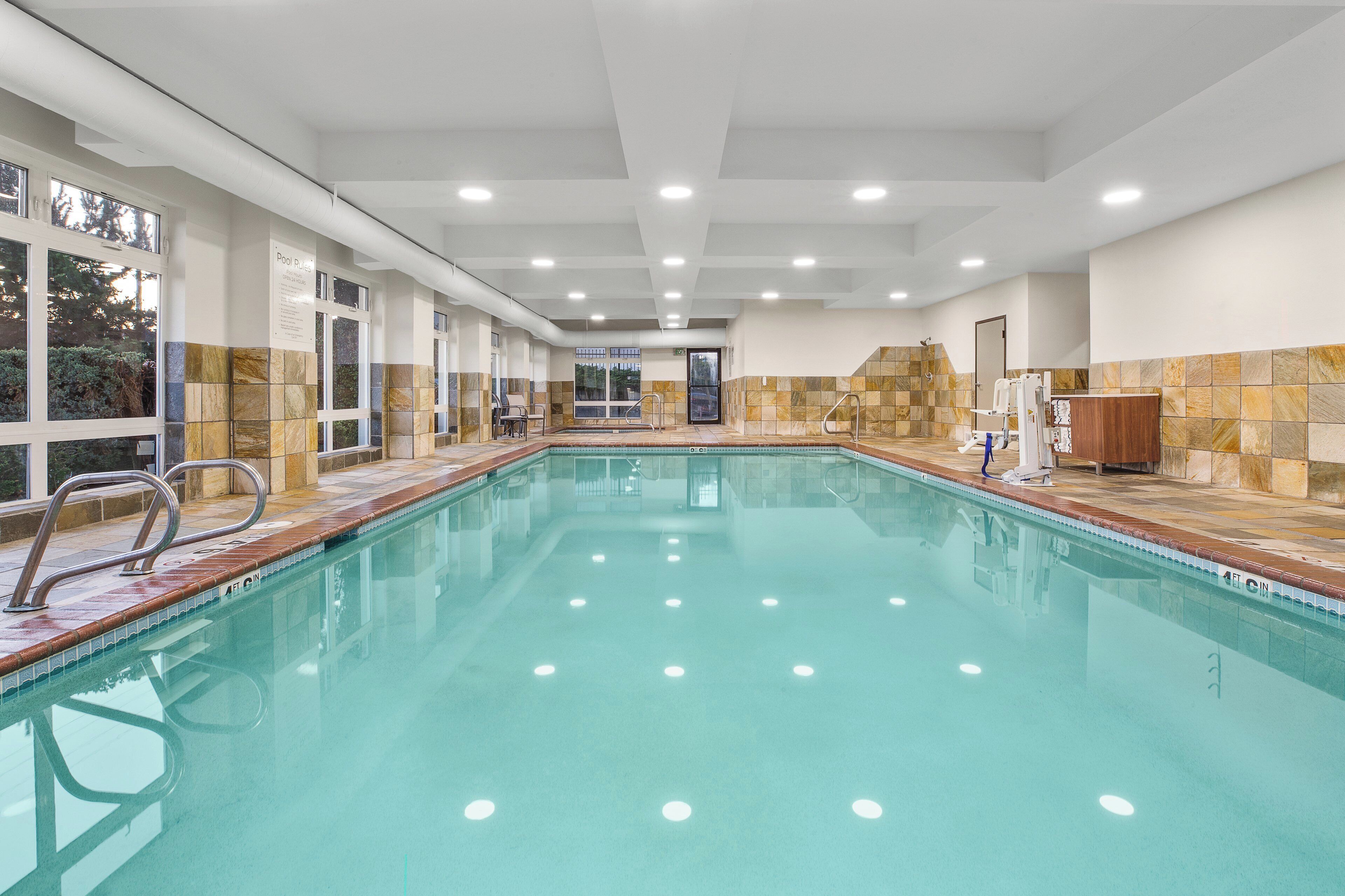 Una amplia piscina interior con agua cristalina, rodeada de paredes con azulejos e iluminación empotrada en el techo.