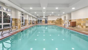 Una amplia piscina interior con agua cristalina, rodeada de paredes con azulejos e iluminación empotrada en el techo.