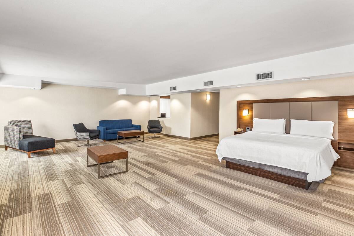 A modern hotel room with a large bed, a sofa, a chair, and a small table.
