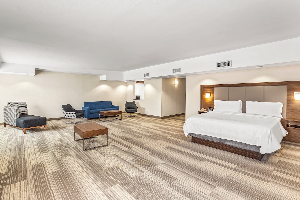 A hotel room with a bed, two armchairs, a sofa, a coffee table, and a carpeted floor.