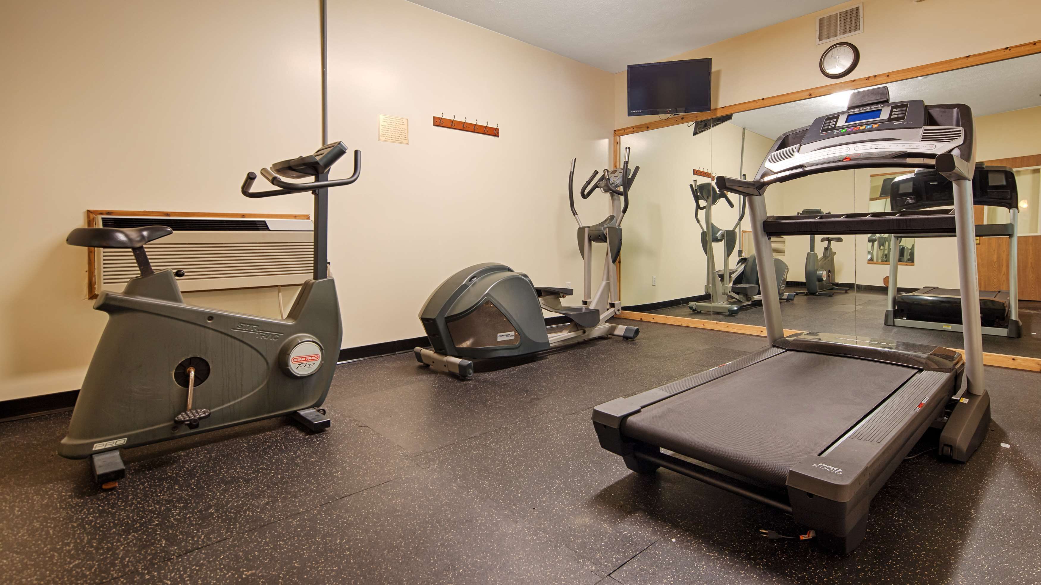 Ein Fitnessraum mit einem Crosstrainer, Laufband und einer Spiegelwand.
