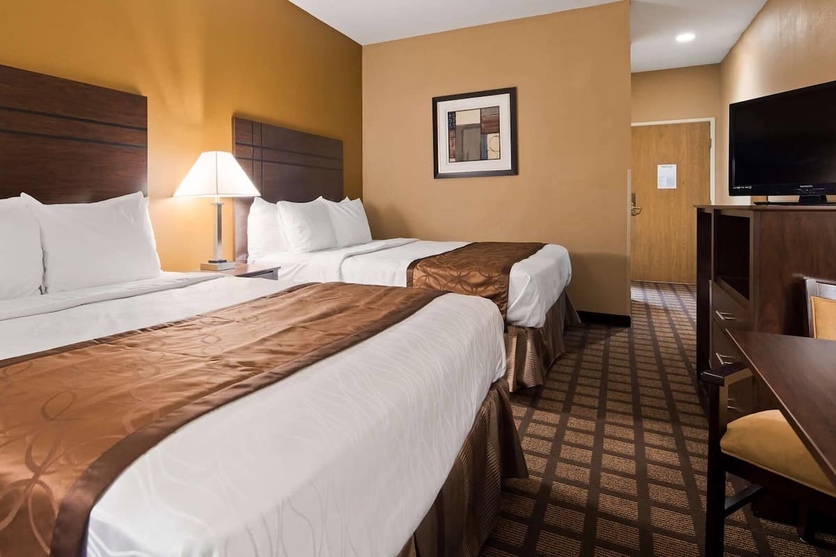 A hotel room with two beds, a desk, a TV, and a framed picture on the wall.