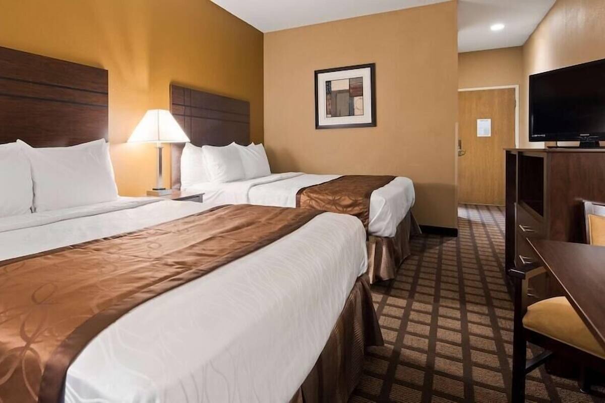 A hotel room with two beds, a desk, a television, and a framed picture on the wall.