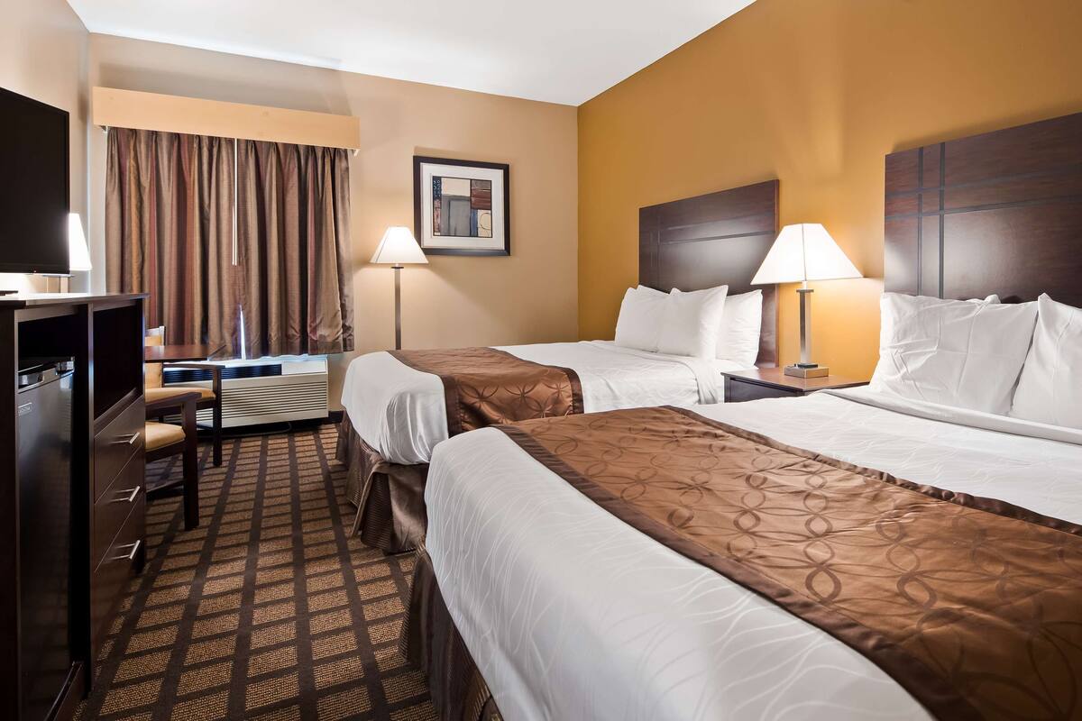 A hotel room with two beds, a desk with a chair, a TV, and a lamp.