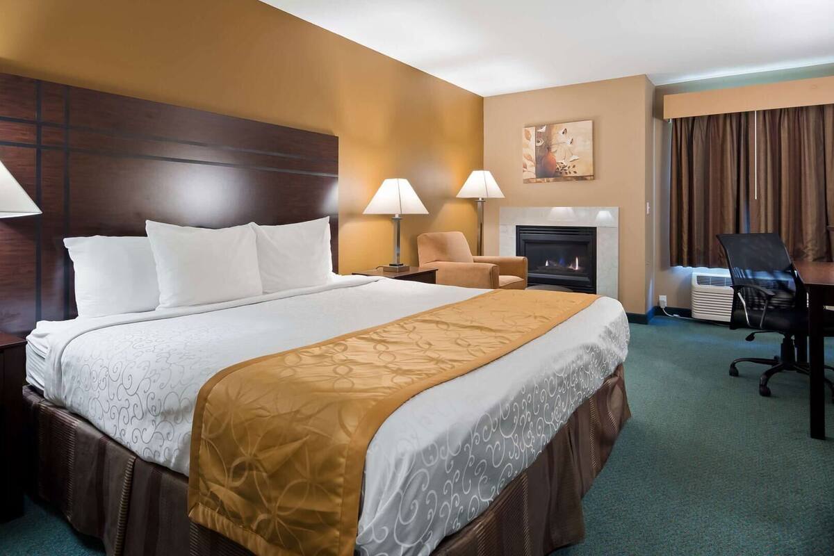 A hotel room with a large bed, two bedside lamps, a chair, a desk, a television, and a fireplace.