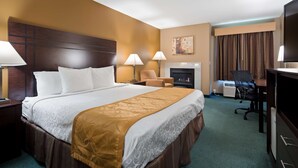 Habitación de hotel con una cama grande, dos lámparas de noche, una silla, chimenea, escritorio con silla y televisor.