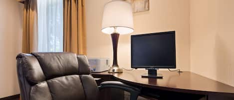Ein Hotelzimmer mit Ledersessel, Schreibtisch, Computerbildschirm, Lampe und einem Fenster mit Vorhängen.