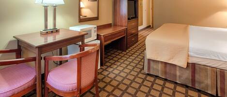 A hotel room with a desk, two chairs, a bed, a television, and a microwave.