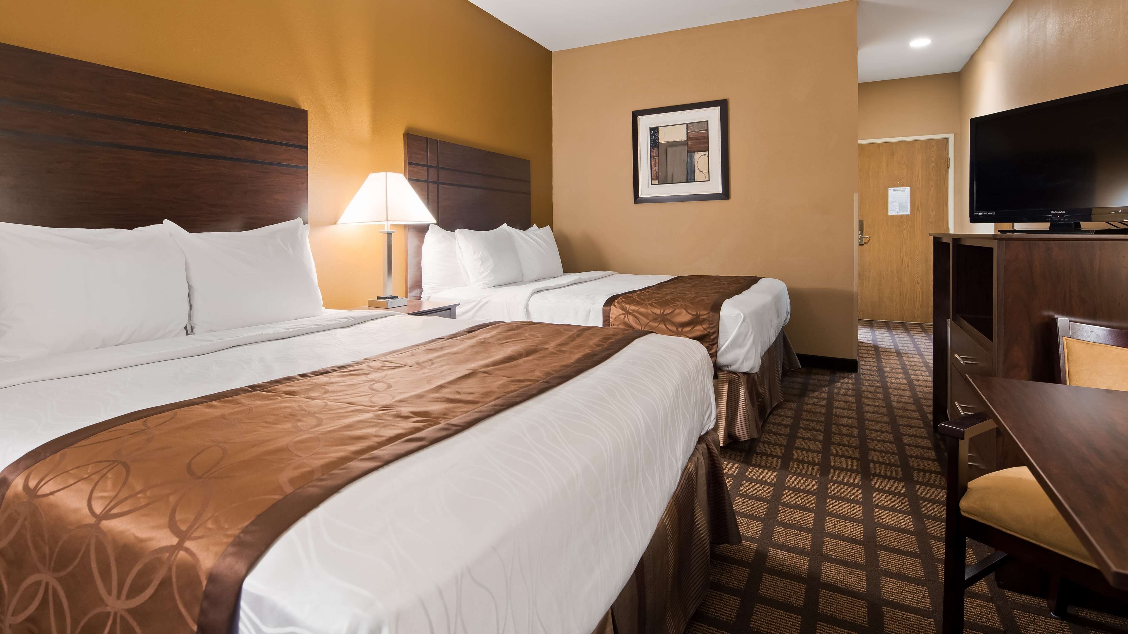 A hotel room with two beds, a desk, a television, and a framed picture on the wall.