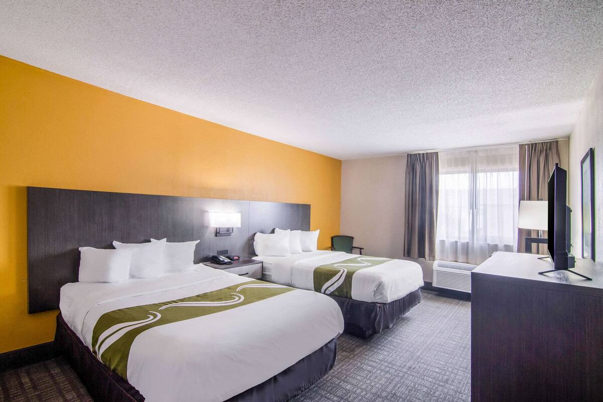 A hotel room with two beds, a desk, a chair, a TV, and a window with curtains.
