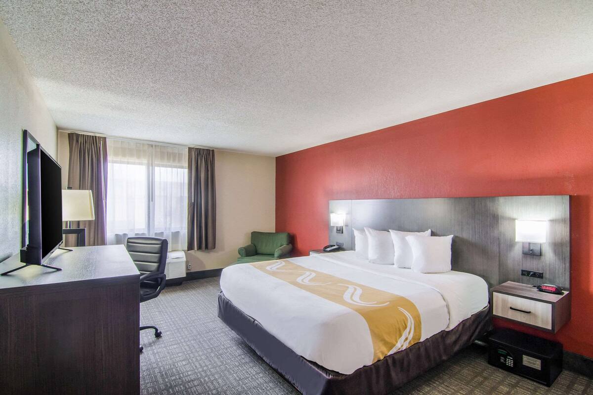 A hotel room with a large bed, a desk with a computer, a chair, and a TV.