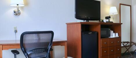 Une chambre d’hôtel équipée d’un bureau, d’un fauteuil de bureau noir, d’un téléviseur posé sur une commode en bois, d’un four à micro-ondes et d’une petite poubelle.