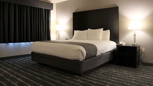 A hotel room with a large bed, two bedside tables with lamps, a dark headboard, and a window with black curtains. - Best Western Fostoria Inn & Suites (Fostoria)