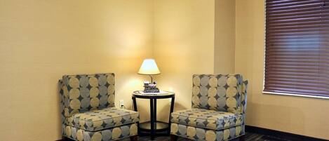 Two armchairs with a geometric pattern, a small round table with a lamp, and a window with blinds.