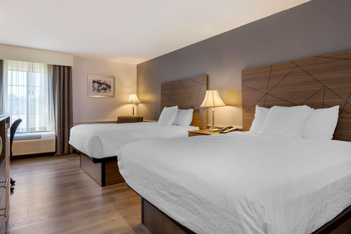 A hotel room with two beds, a desk, and a window with curtains.