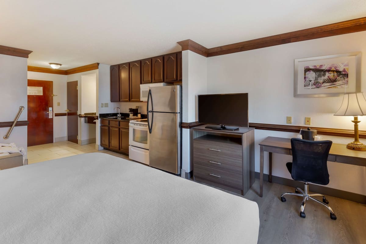 A hotel room with a bed, kitchenette, desk, and chair.
