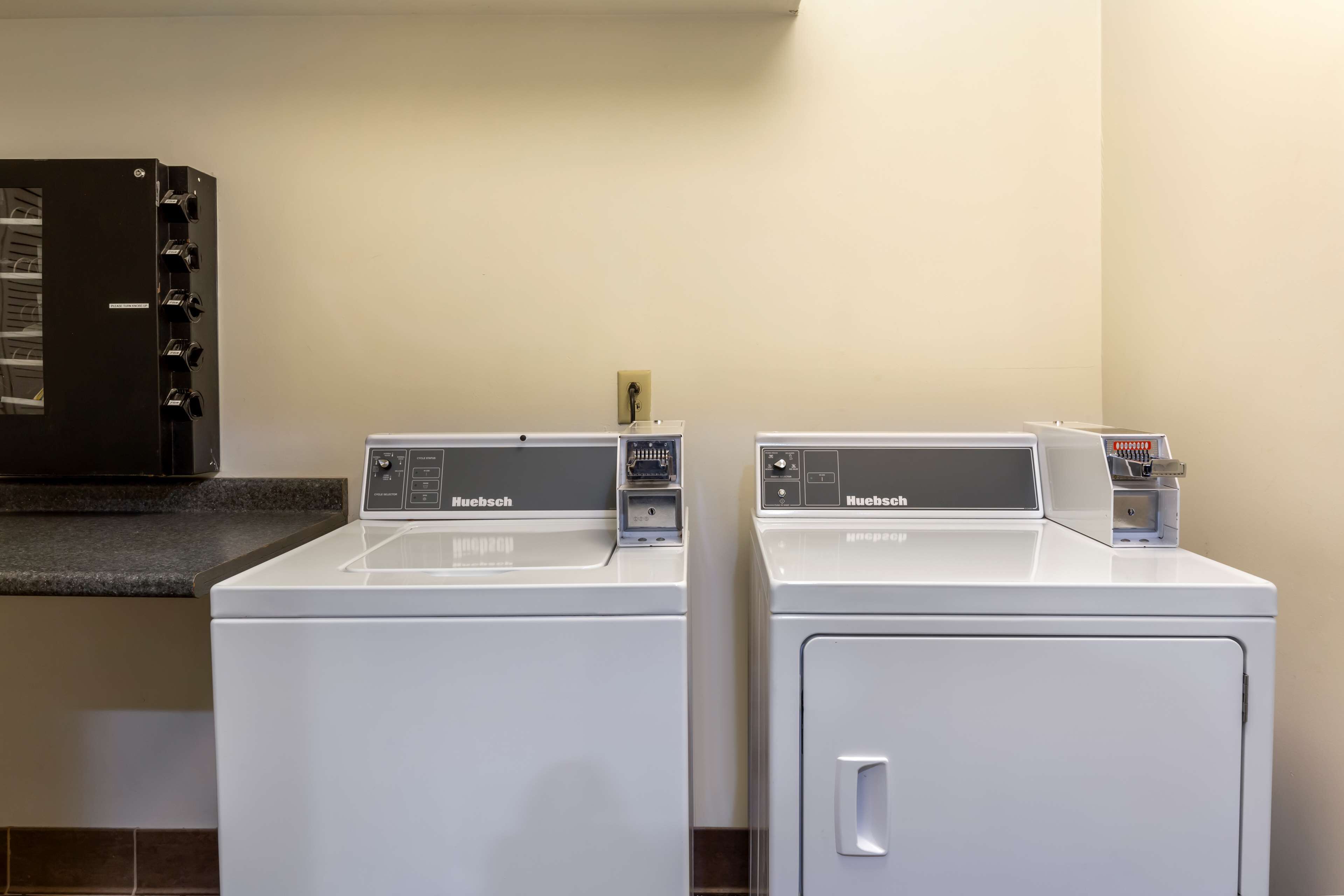 Two white Huebsch brand front-loading washing machines in a laundry room with a black cabinet above.