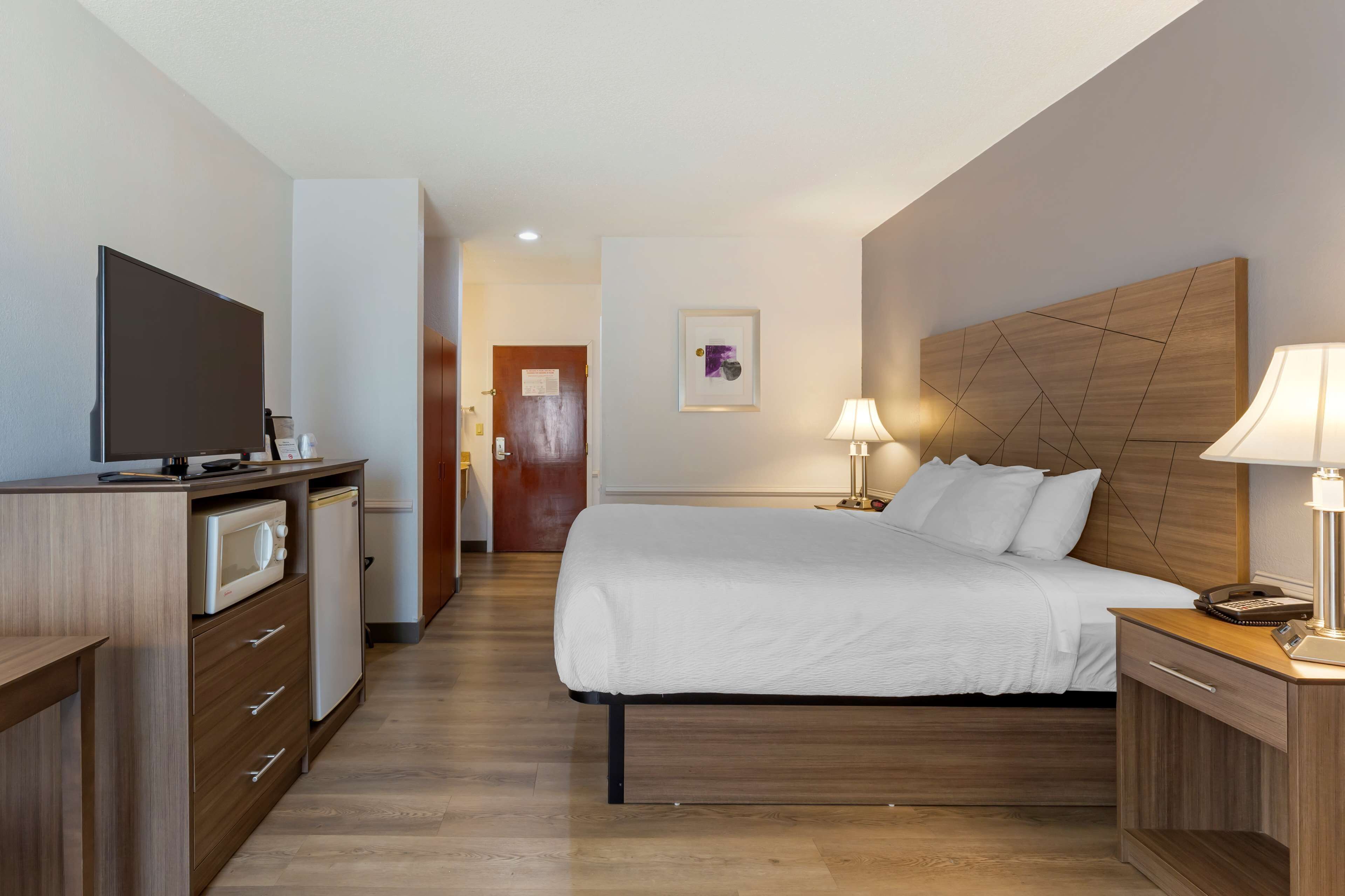 Een moderne hotelkamer met een bed, nachtlampjes, een televisie, een magnetron en een houten hoofdeinde.