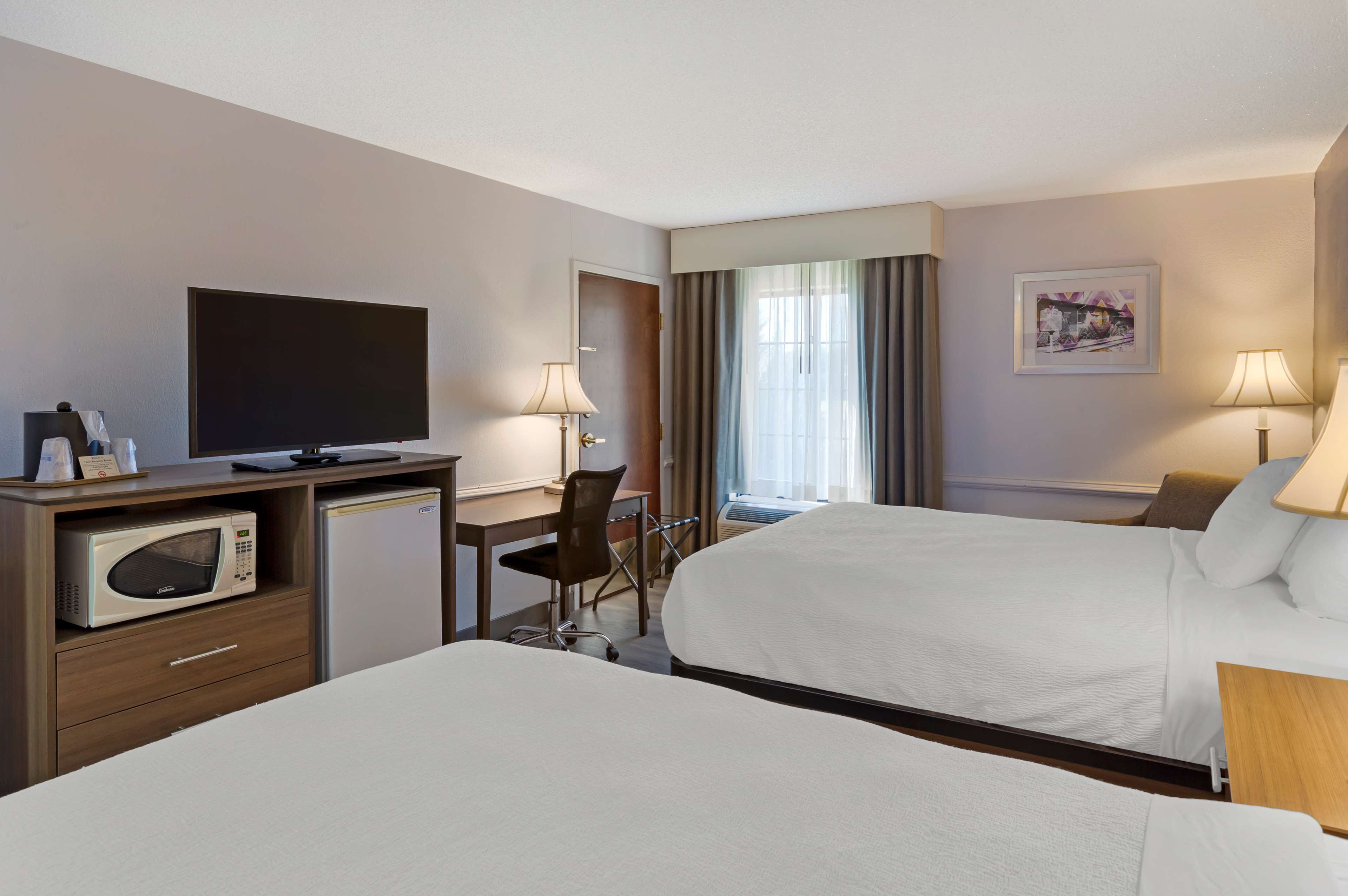Een hotelkamer met twee bedden, een bureau met een magnetron, een televisie en een stoel.