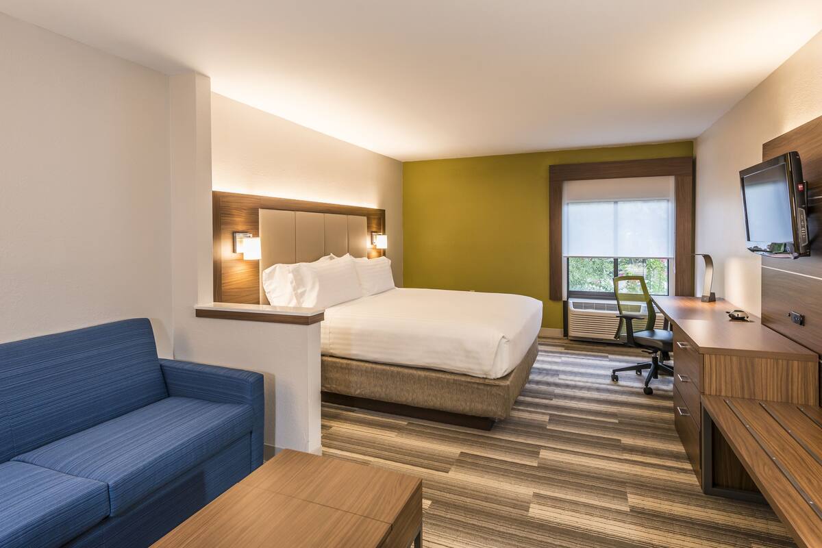 Habitació d'hotel amb llit, un sofà blau, escriptori de fusta, televisió i finestra amb vistes.