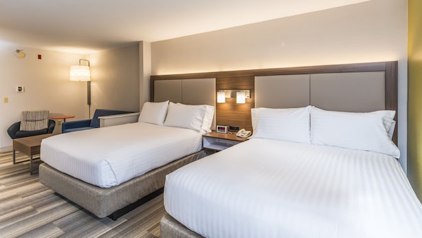 A hotel room with two beds, a bedside table, a lamp, and a clock.