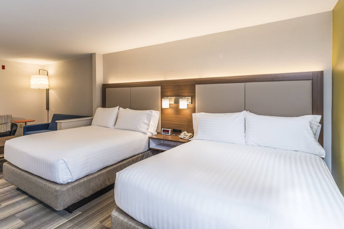 Habitació d'hotel amb dos llits, una taula de nit, una làmpada i un rellotge.