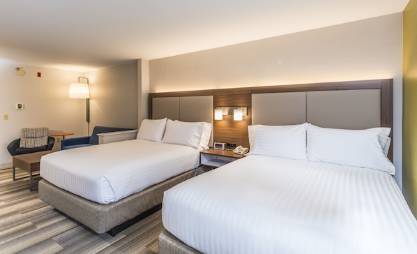Quarto de hotel com duas camas, mesa de cabeceira, luminária e relógio.