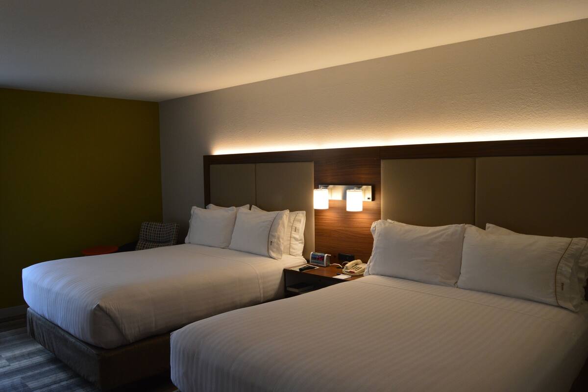 Habitació d'hotel amb dos llits, un panell de capçalera de fusta, làmpades de sobretaula i una taula de nit amb un telèfon i un comandament a distància.