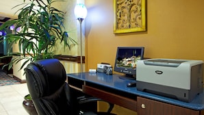 A hotel office with a desk, computer, printer, and a potted plant.
