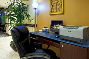 Um balcão de hotel com computador, impressora e uma planta em vaso.
