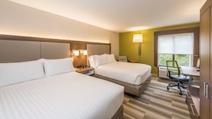 A hotel room with two beds, a desk, a chair, and a window with a view of greenery.