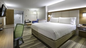 A hotel room with a large bed, a desk with a chair, a TV, and a bedside table with a lamp.