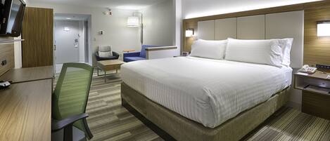 A hotel room with a large bed, a desk with a chair, a TV, and a bedside table with a lamp.
