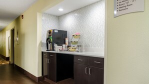 Pasillo de hotel con un área de kitchenette que incluye una máquina de hielo, cafetera y un frutero en un estante.