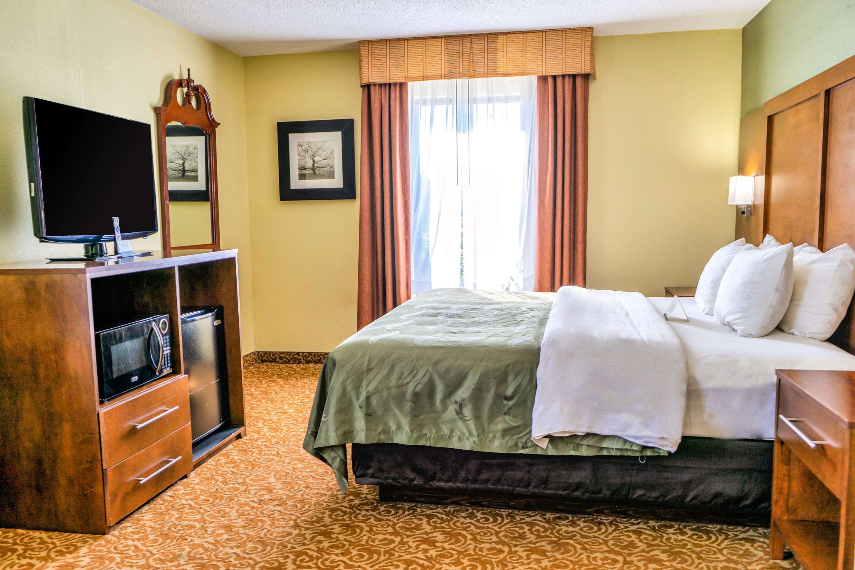A hotel room with a bed, a television, a dresser, and a window with curtains.
