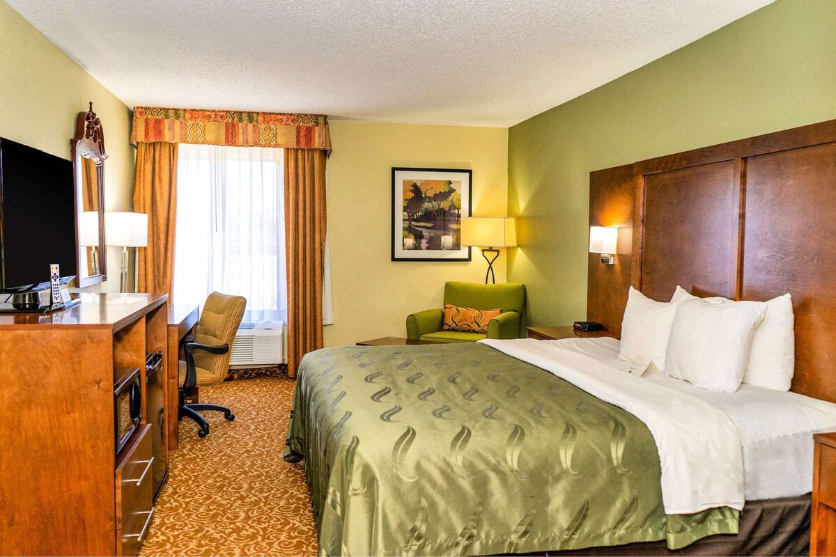 Une chambre d’hôtel avec un lit, un bureau, une chaise, une télévision et une fenêtre avec des rideaux.