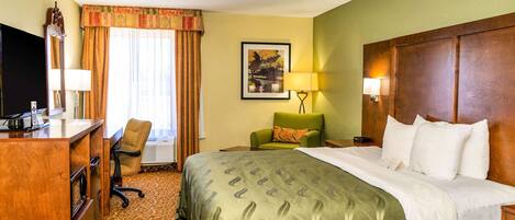A hotel room with a bed, a desk, a chair, a TV, and a window with curtains.