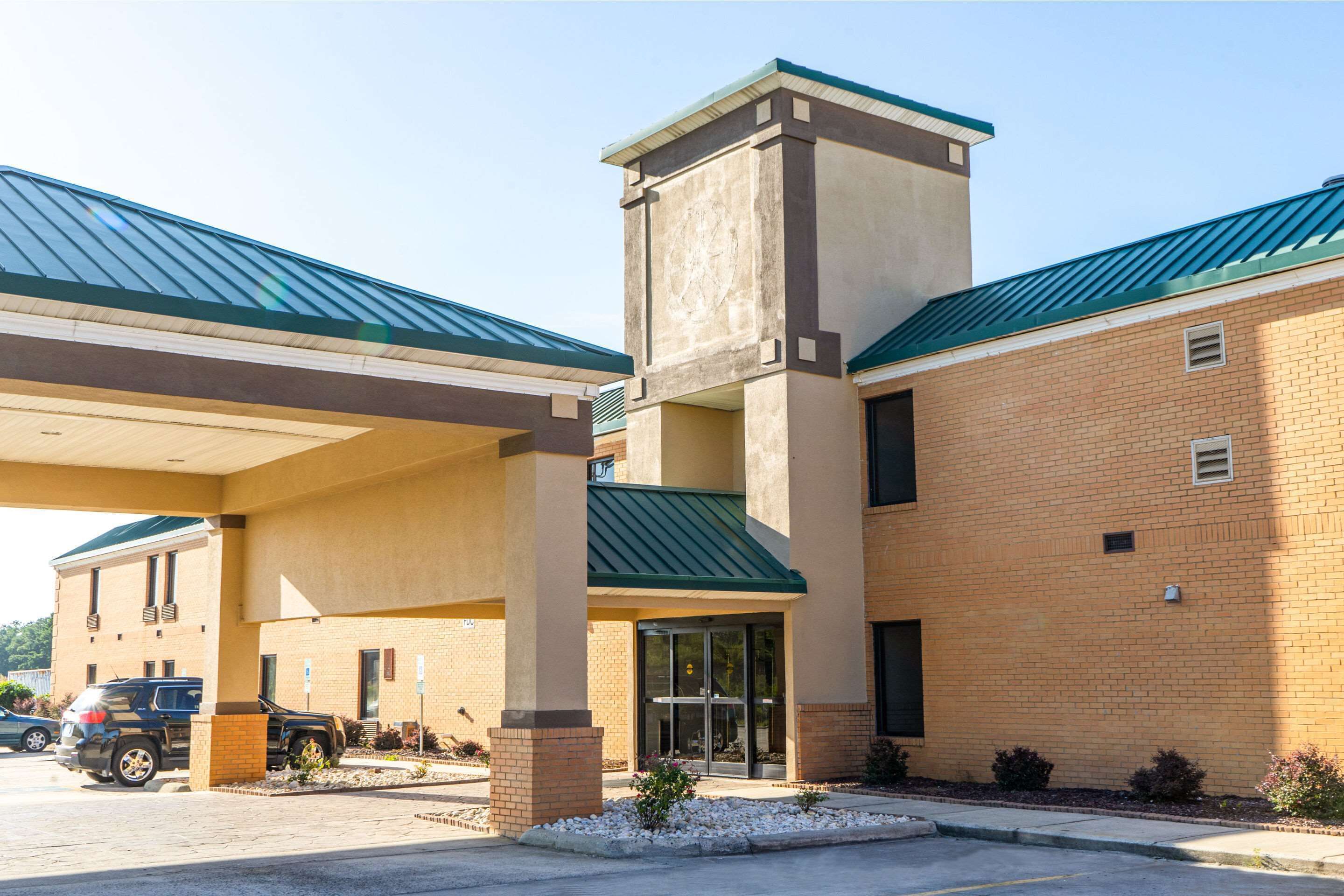 A hotel with a brick facade, a green roof, and a covered parking area.