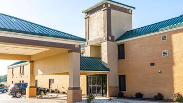 A hotel with a brick facade, a green roof, and a covered parking area.