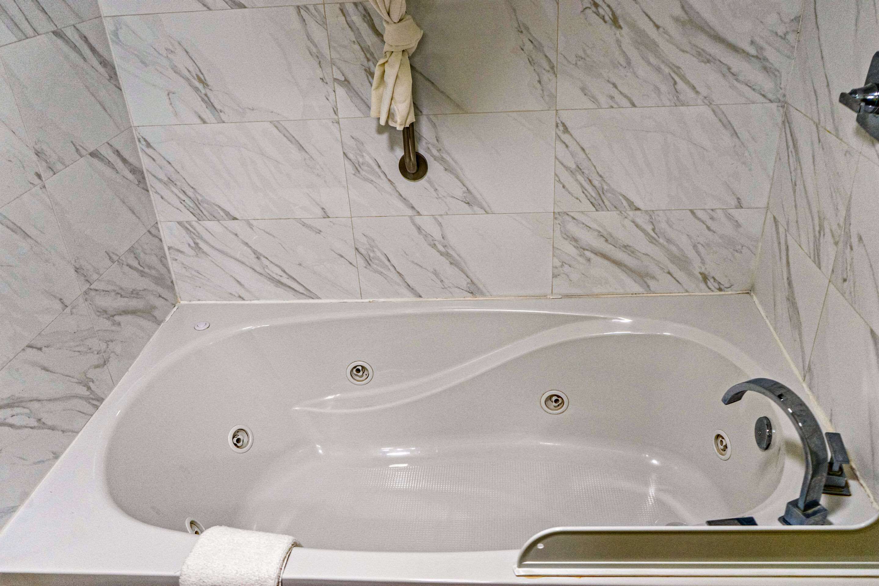 A bathroom with a large bathtub, a towel rack, and a marble tiled wall.