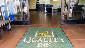 Entrada de un hotel con un felpudo verde que muestra el nombre 'Quality Inn Whiteville, NC'.