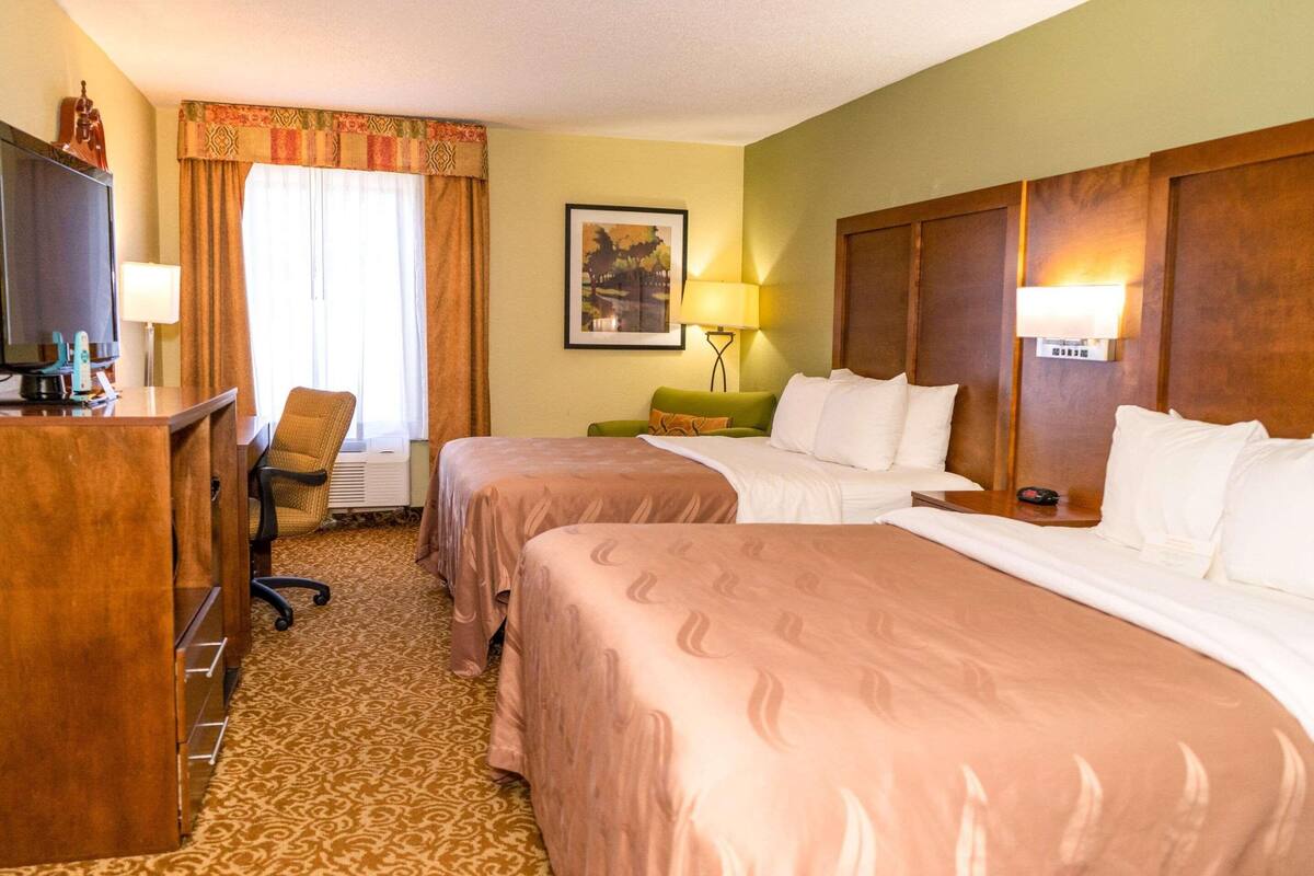 Une chambre d’hôtel avec deux lits, un bureau avec une télévision, une chaise, une lampe et un tableau encadré au mur.