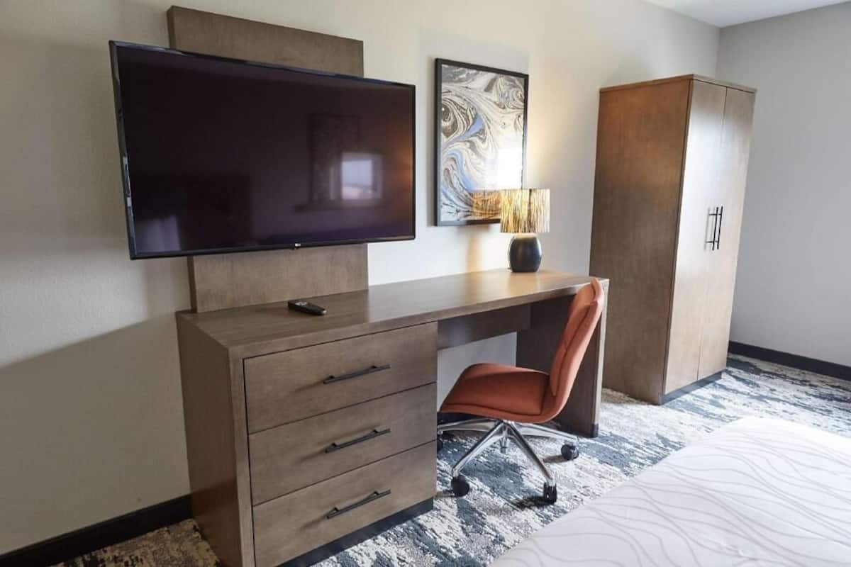 Une chambre d’hôtel équipée d’une télévision à écran plat, d’un bureau avec des tiroirs, d’une chaise, d’une lampe et d’une armoire.