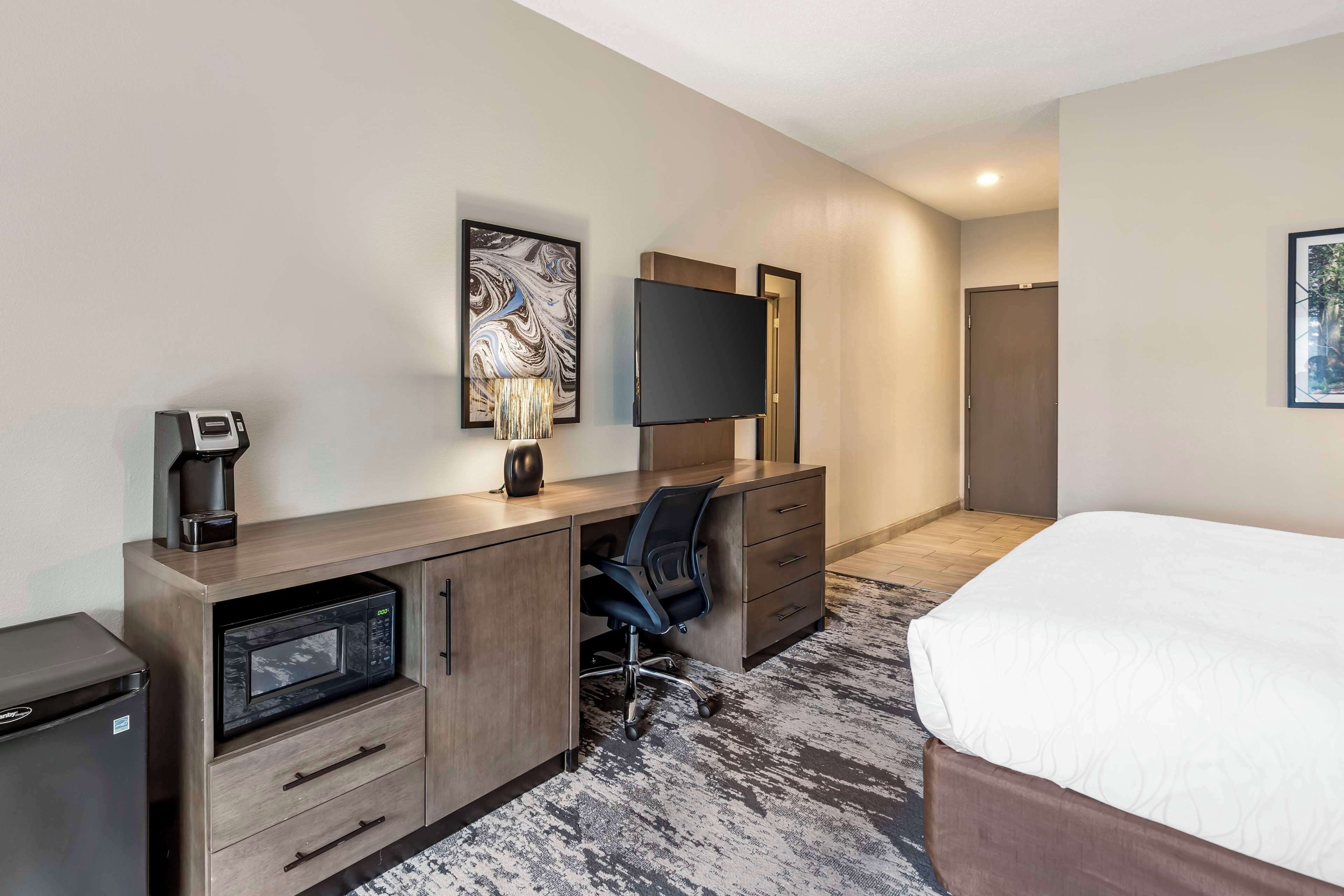 A hotel room with a bed, a desk with a microwave, a chair, a TV, and a coffee maker.